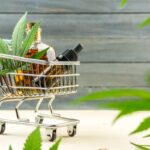 Supermarket trolley with marijuana leafs and medical cannabis oil cbd on wooden backdrop