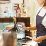 Cropped image of female barista working at dispensary and using cash register when accepting payment or entering order details